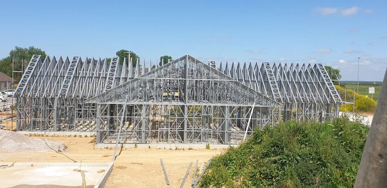 Structure en cours de construction avec une charpente métallique sous un ciel bleu.